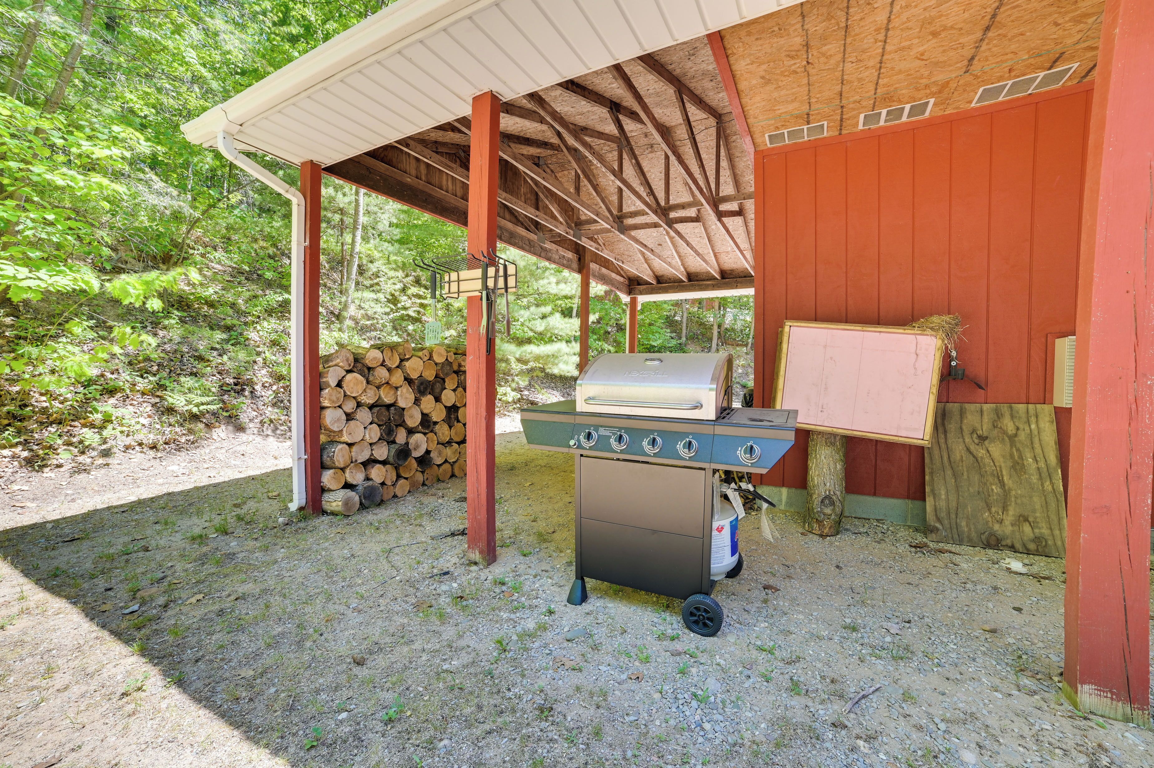 An outdoor barbecue area with a grill, a stack of firewood, and a covered shelter.