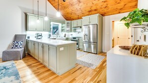Une cuisine moderne avec un plafond en bois, des meubles de couleur vert clair, des appareils électroménagers en acier inoxydable et un îlot central.