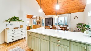 Une cuisine spacieuse dotée d’un grand îlot central, d’un plafond en bois et bénéficiant d’un éclairage naturel abondant.