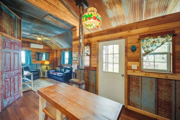 A rustic cabin interior with a wooden dining table, leather sofas, and a ceiling fan.