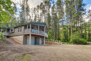 A two-story cabin with a balcony, surrounded by a forest.