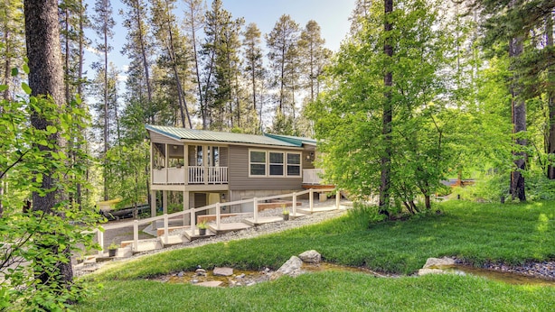 A cabin with a deck, surrounded by a forest and a small stream.