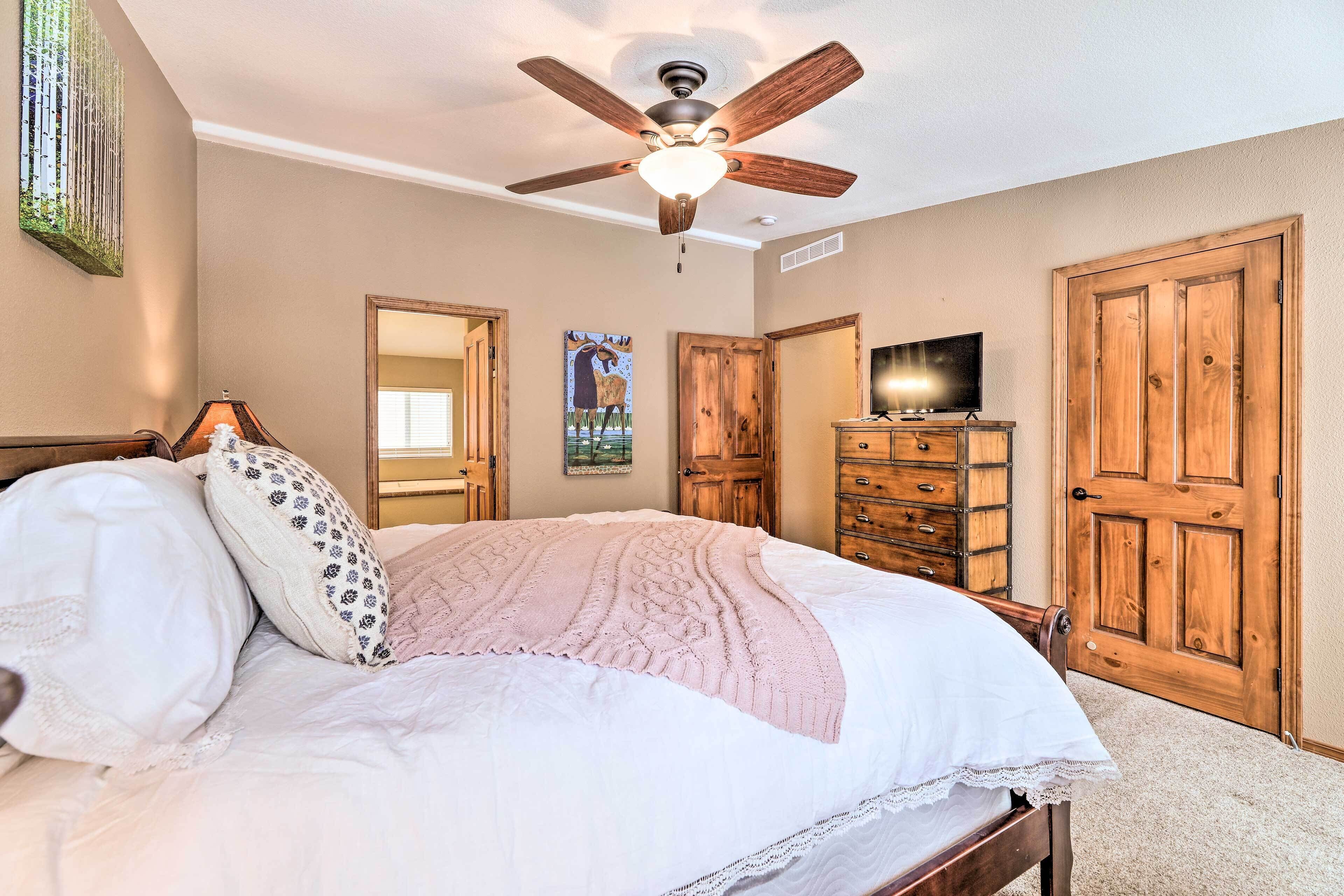 A bedroom with a bed, a ceiling fan, wooden doors, a dresser, and a television.