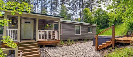 A two-story cabin with a front porch, a deck, and a hot tub.