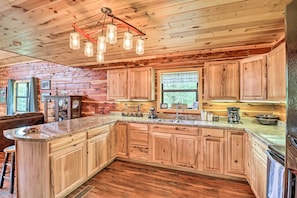 A spacious kitchen with wooden cabinets, a large island, and a farmhouse-style ceiling. - Rural Wooded Cabin Near Trophy Trout Fishing! (Norfork)