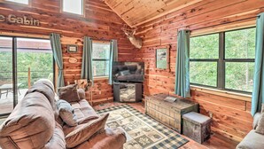 Interior d'una cabana amb una televisió gran, seients confortables, un corró de ciervo muntat i grans finestres.