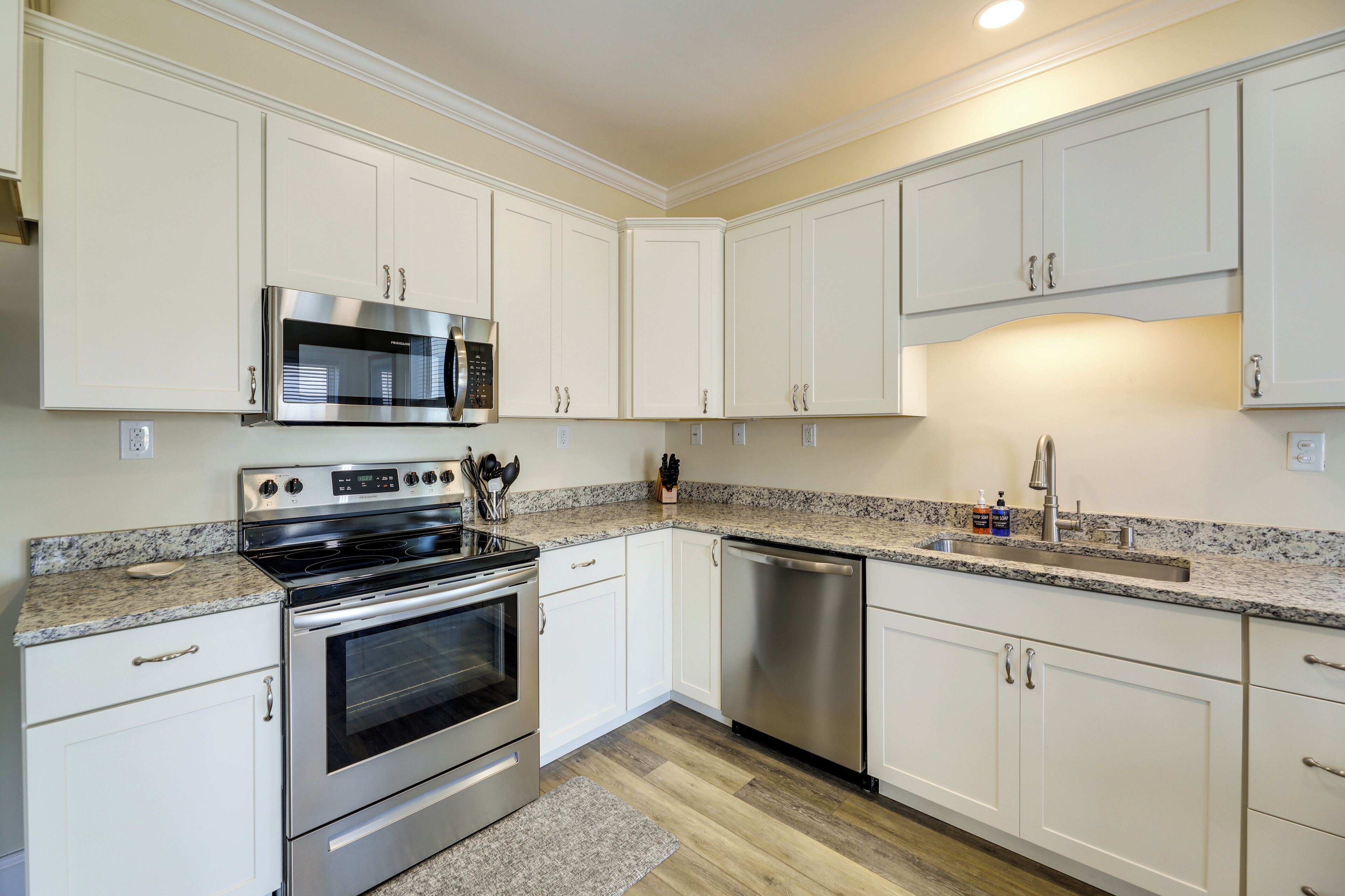 A modern kitchen with white cabinetry, stainless steel appliances, granite countertops, and a granite backsplash.