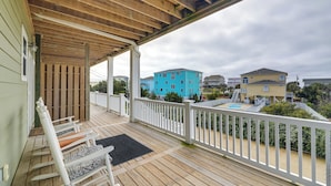 Eine Holzterrasse mit weißer Brüstung, eine überdachte Veranda und Blick auf angrenzende Häuser.
