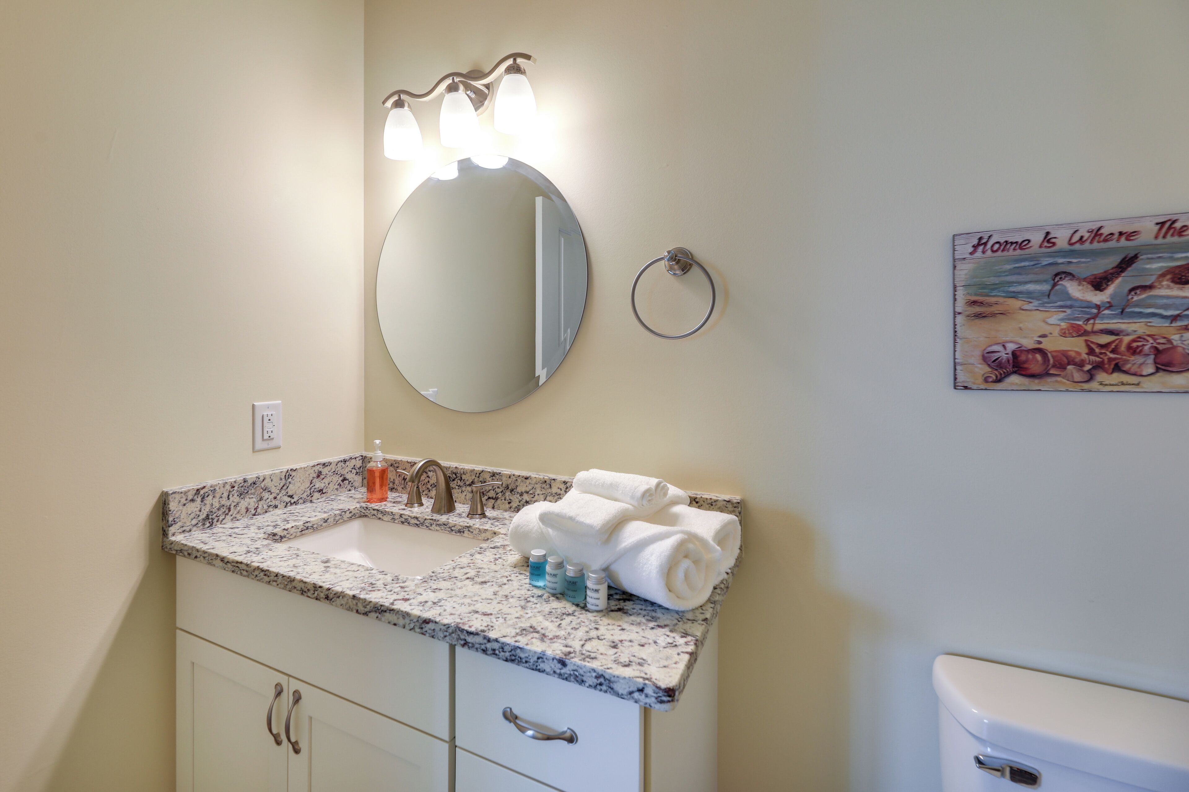 A bathroom with a marble sink, a round mirror, and a toilet. There are towels and toiletries on the sink.