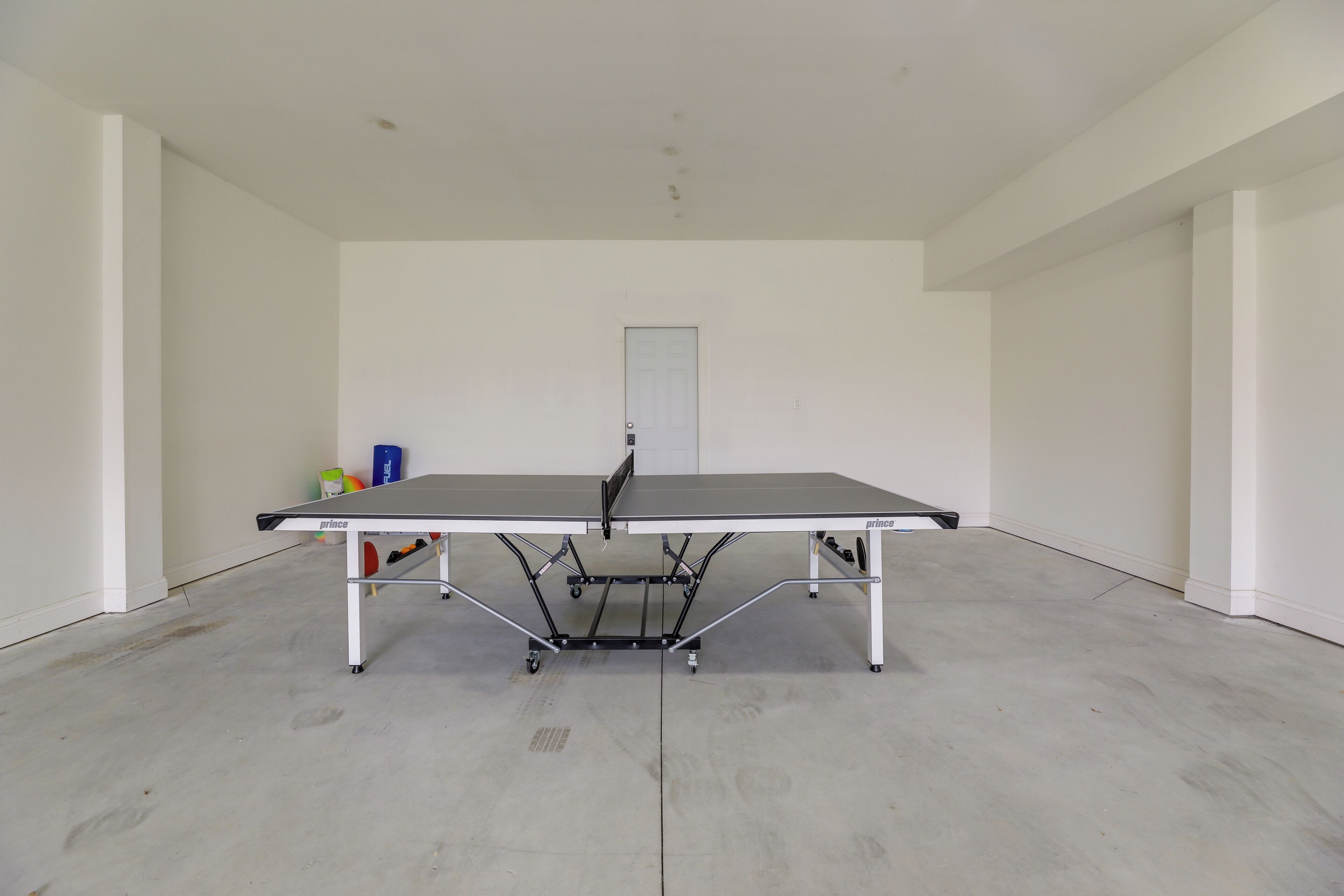 Une table de ping-pong dans une pièce aux murs blancs, avec une porte visible au fond.
