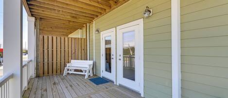 A covered porch with a wooden ceiling, a white bench, and a door with a glass panel.