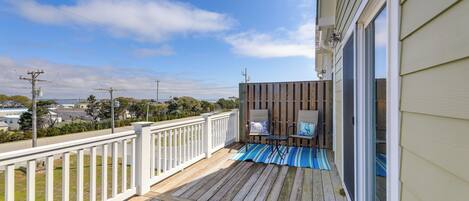 A wooden deck with a white railing, a covered seating area with a table and chairs, and a view of the surrounding neighborhood.