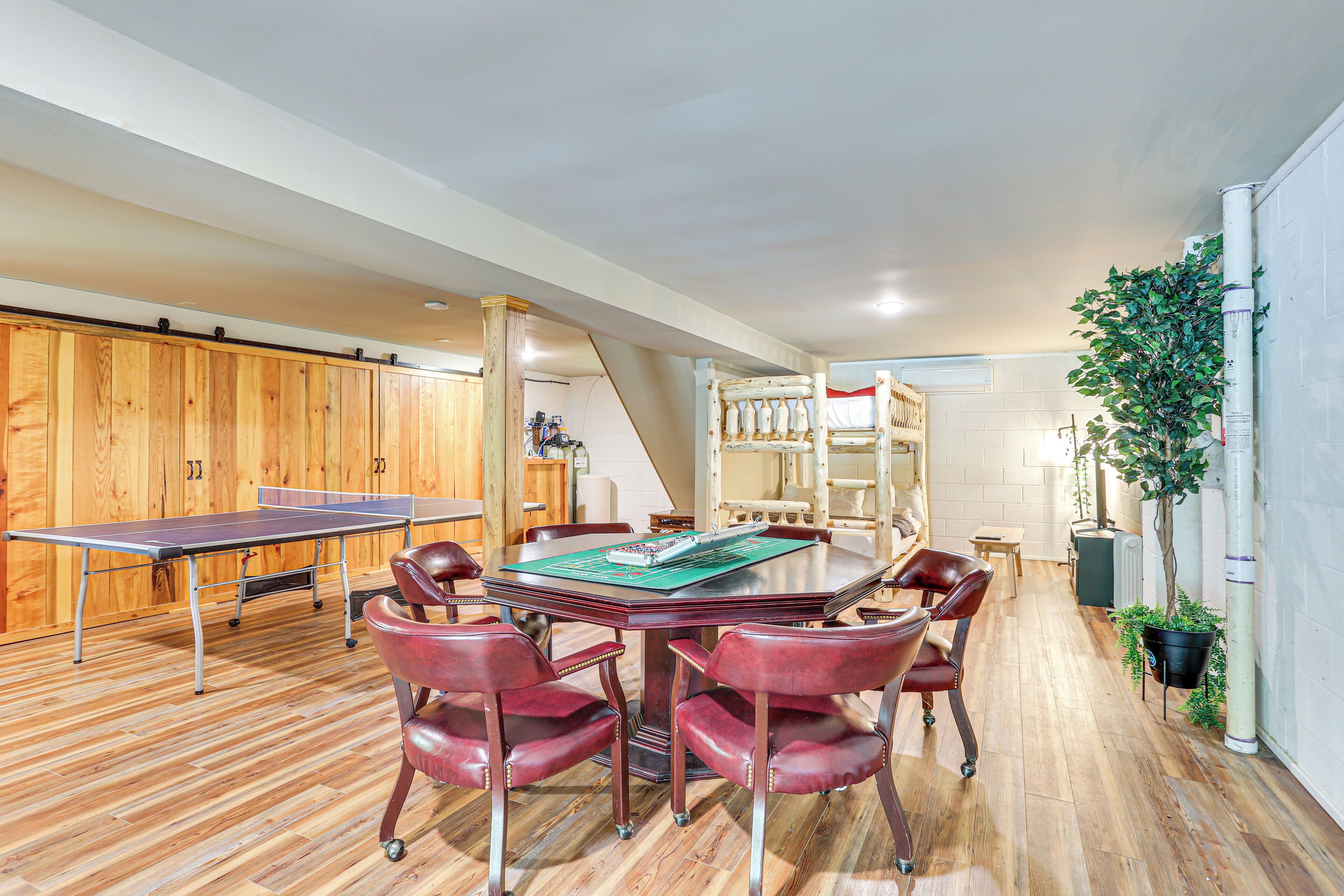 A spacious room with a ping pong table, a wooden cabinet, a staircase, and a potted plant.