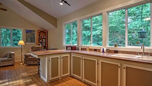 A spacious kitchen with a large window, wooden cabinets, and a built-in sink. - Harbert Cottage w/ Fire Pit: Half Mile to Beach! (Harbert)
