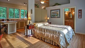 A bedroom with a large bed, a desk, and a chair. There is a window with a view of trees, a ceiling fan, and a mirror. - Harbert Cottage w/ Fire Pit: Half Mile to Beach! (Harbert)
