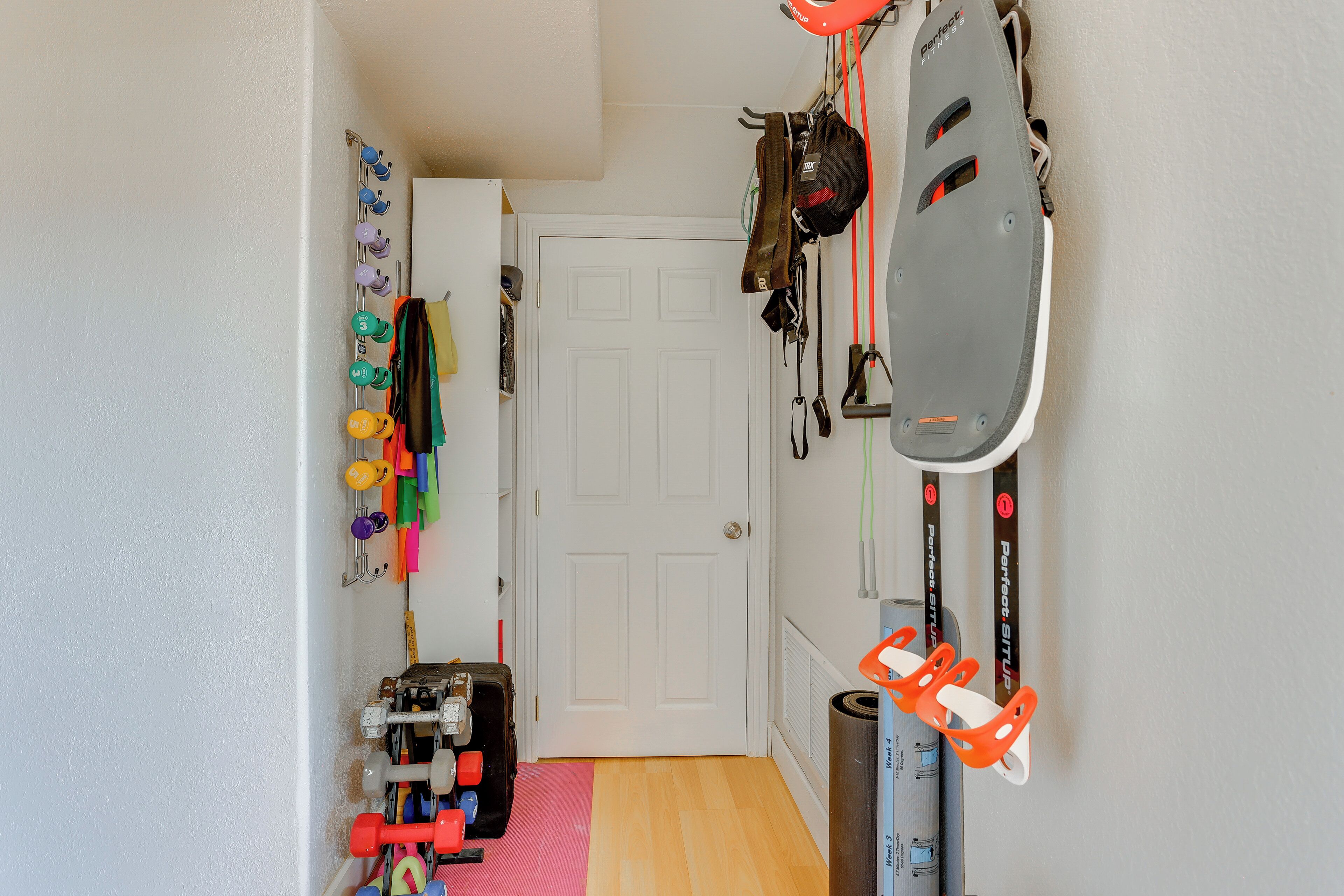 A hallway with a white door, a pink mat, and various items like dumbbells, a helmet, and a bike rack.