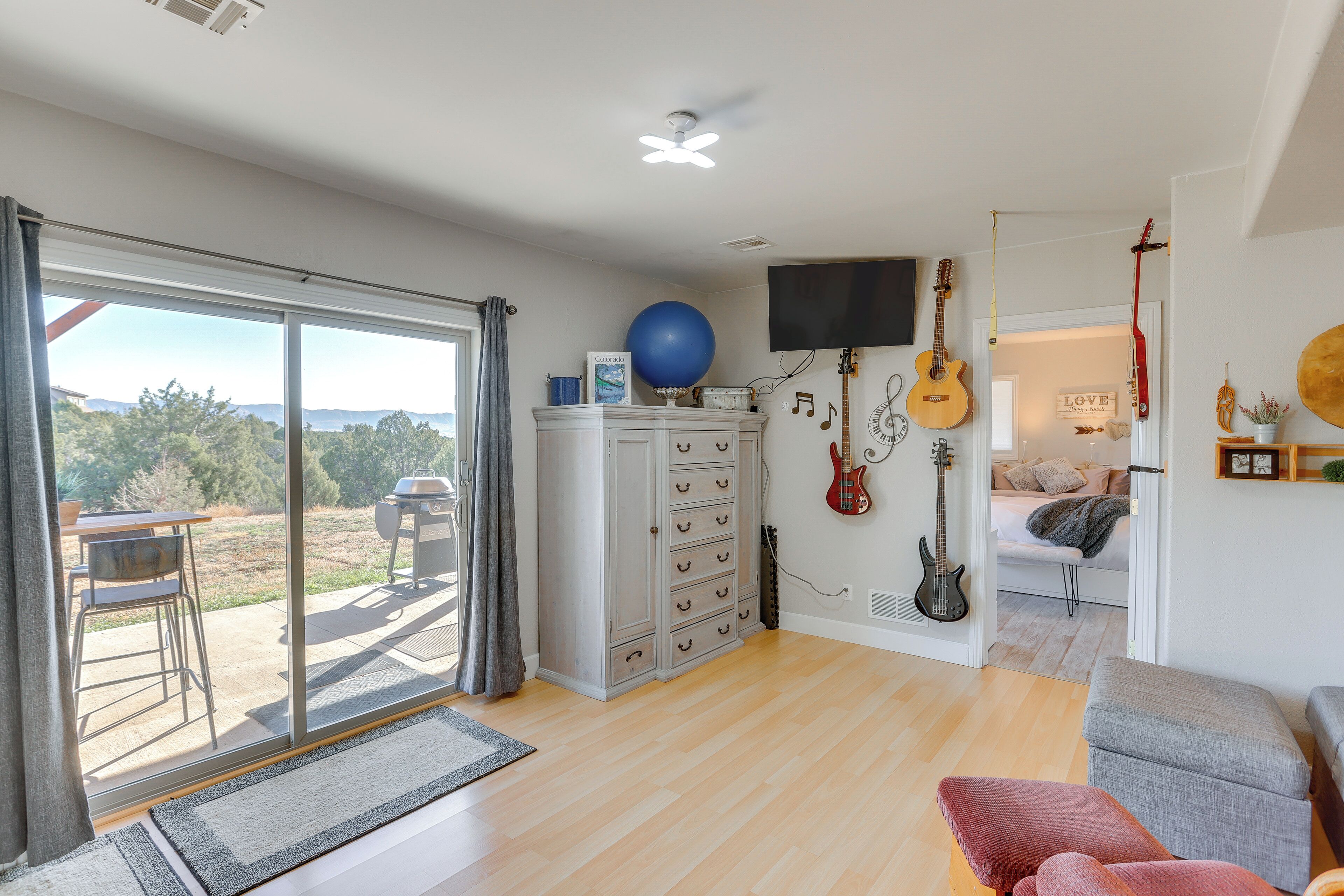 A spacious living room with a sliding glass door leading to an outdoor patio, a flat-screen TV mounted on the wall, and a guitar hanging on the wall.