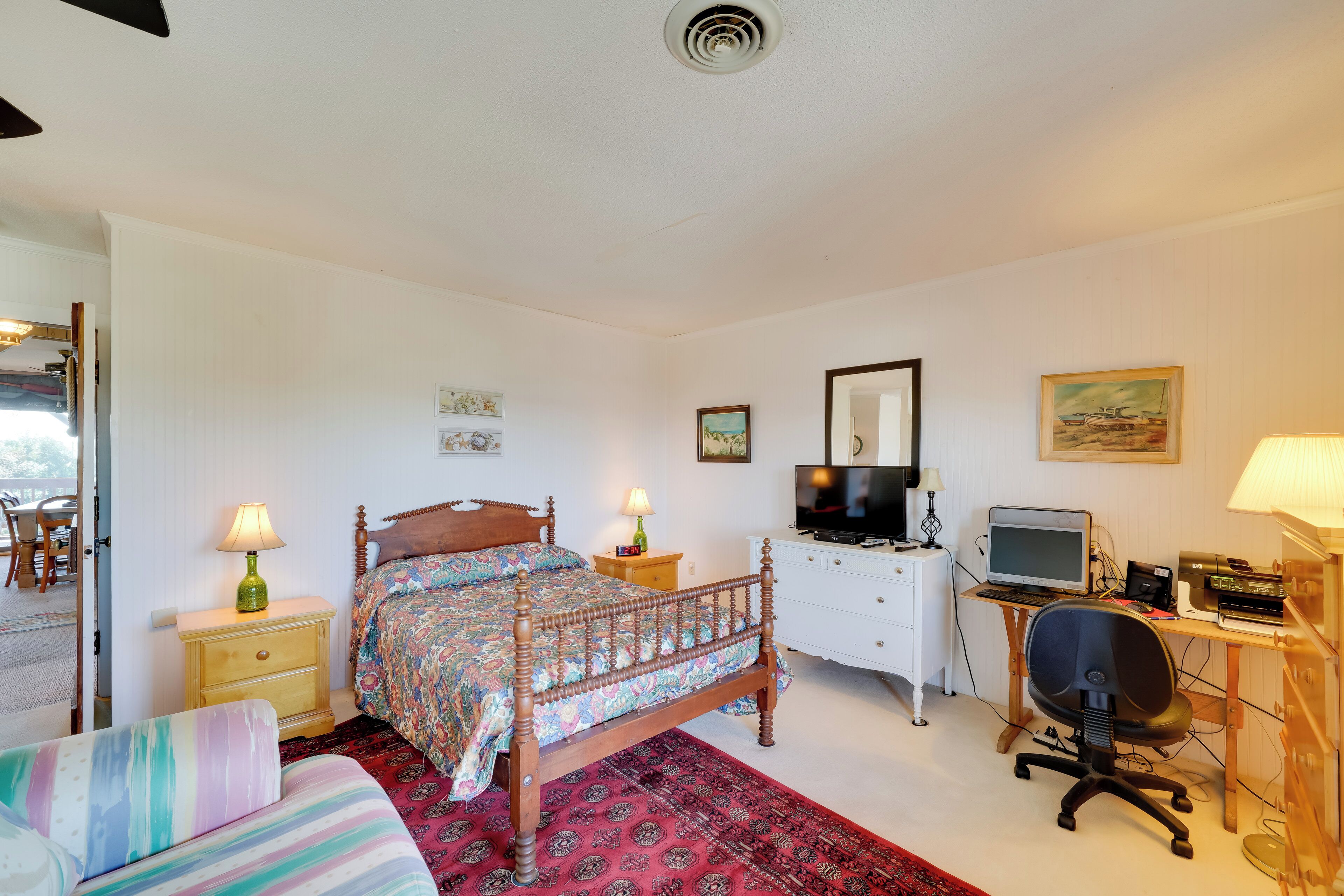 Une chambre à coucher avec un lit en bois, un bureau avec un ordinateur, une chaise, une télévision et une lampe.