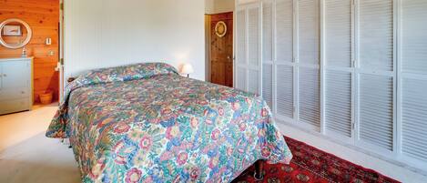 Un dormitorio con una cama, un ventilador de techo, una puerta de madera y un armario con contraventanas blancas.