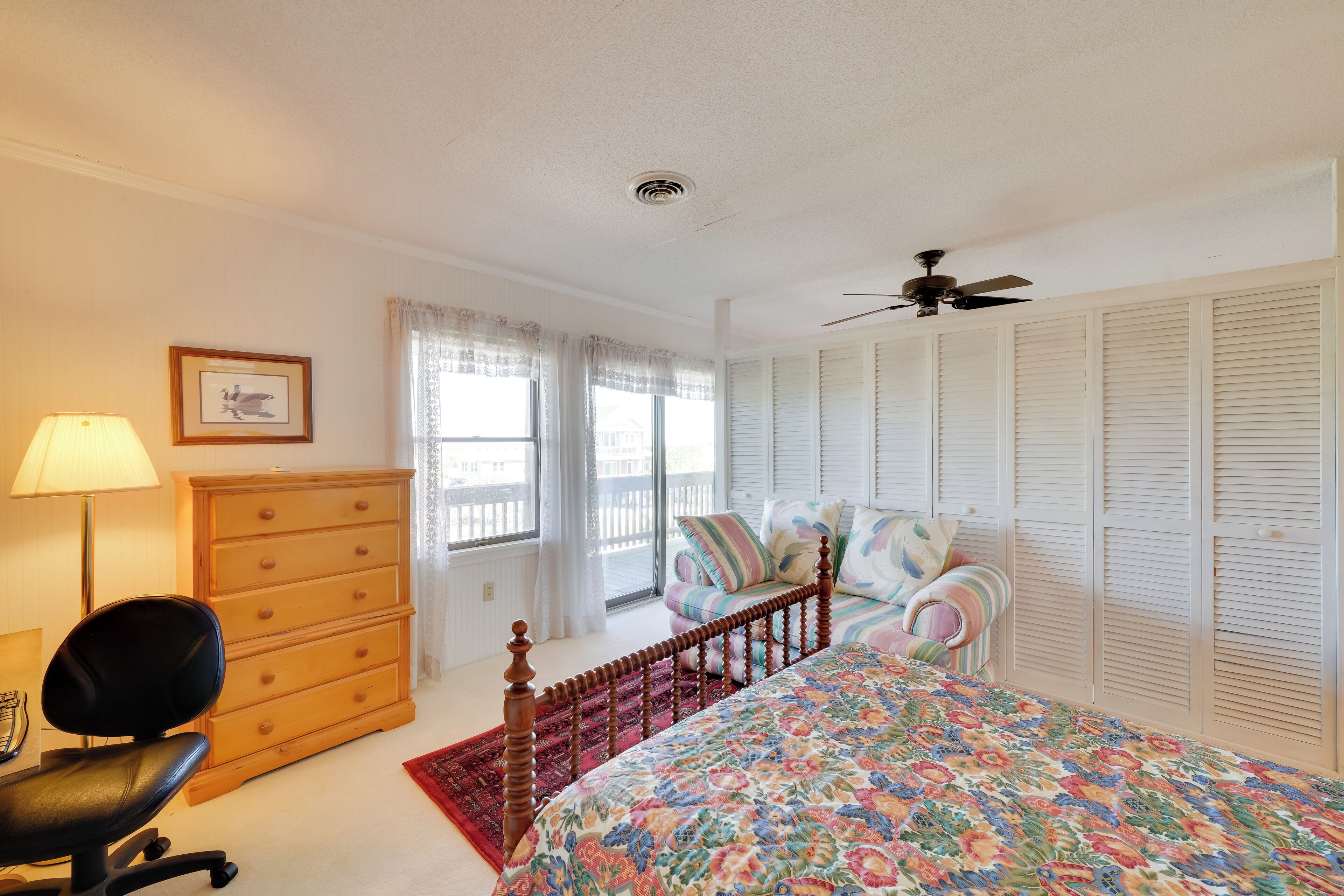 A bedroom with a bed, dresser, chair, and a ceiling fan.