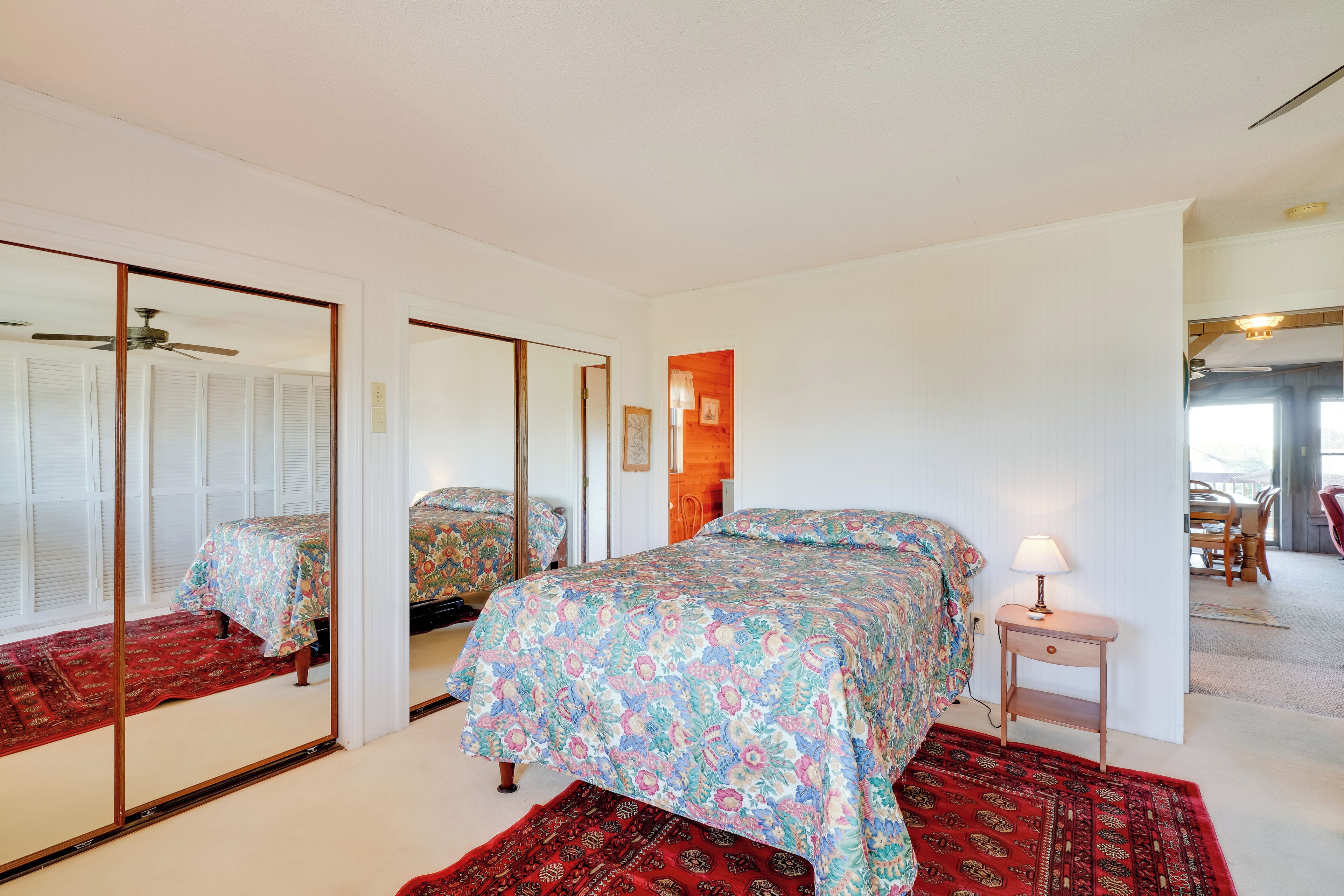 A bedroom with a bed, a nightstand, a mirror, and a red rug.