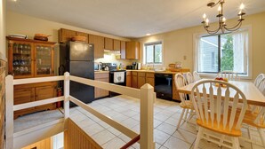 A kitchen with wooden cabinets, a black refrigerator, a dining table with white chairs, and a chandelier. - Dover Condo w/ Grill & Balcony: 3 Mi to Mt Snow! (West Dover)
