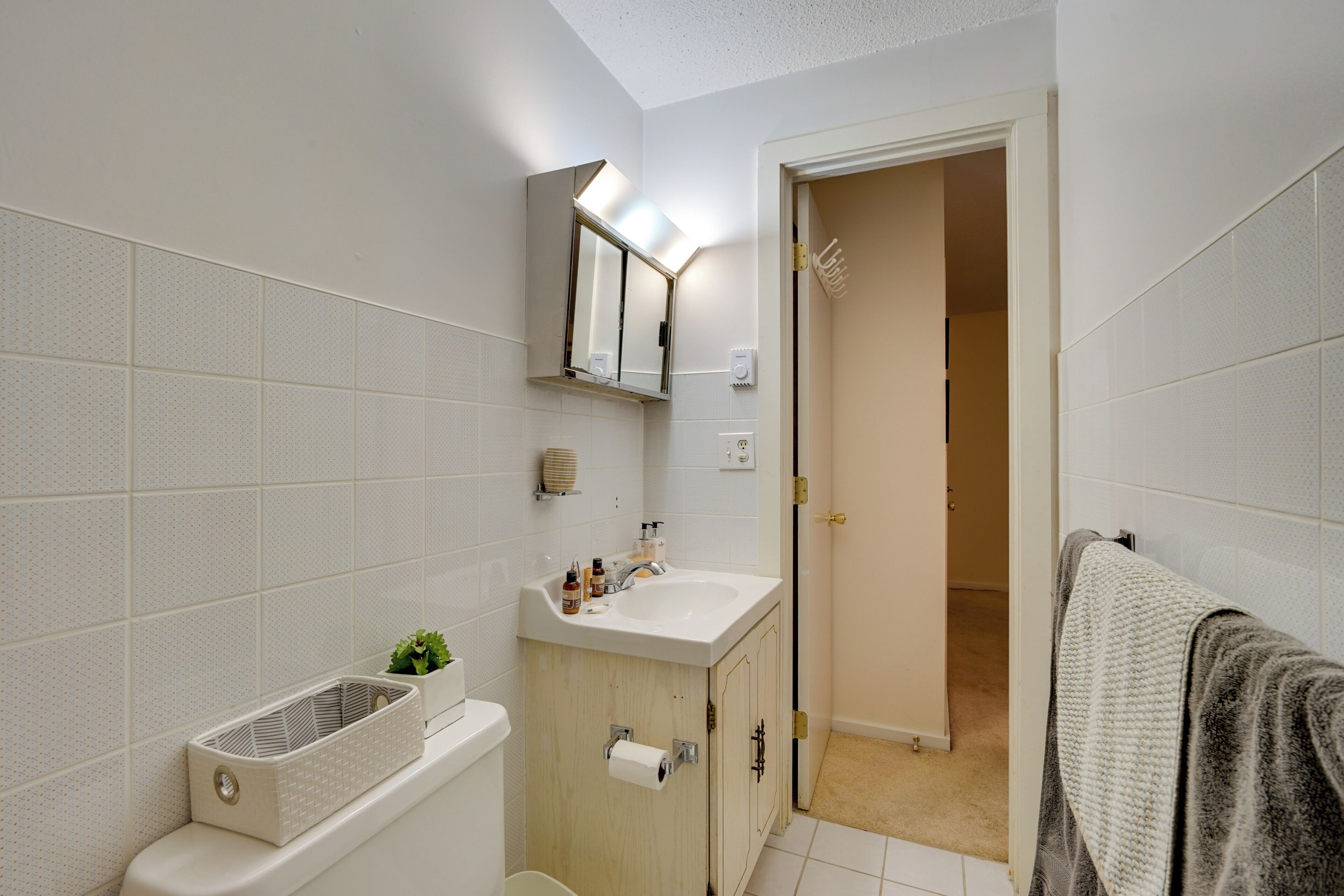 Een badkamer met een wit wastafelmeubel, spiegel en toilet. Er hangt een handdoek aan de muur.