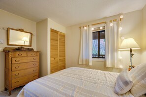 Een slaapkamer met een bed, een kaptafel, een spiegel, een raam met gordijnen en een lamp.