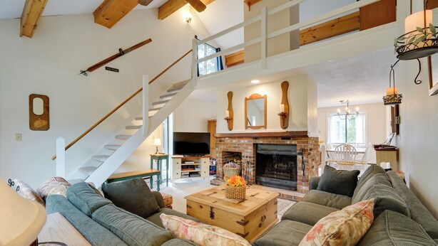 A spacious living room with a large sofa, a fireplace, a staircase, and a television. - Dover Condo w/ Grill & Balcony: 3 Mi to Mt Snow! (West Dover)
