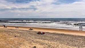 Uma praia com areal, algumas pessoas e um veículo vermelho.