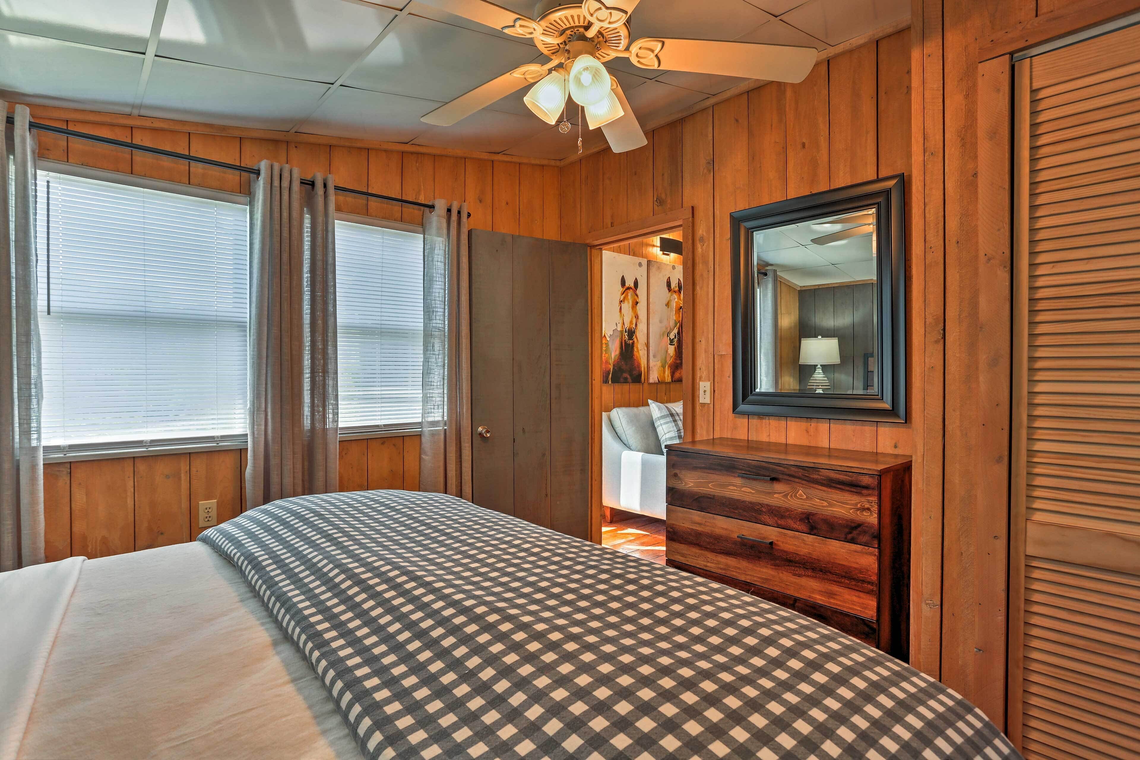 Een slaapkamer met een bed, houten wanden, een plafondventilator, een dressoir en een spiegel.