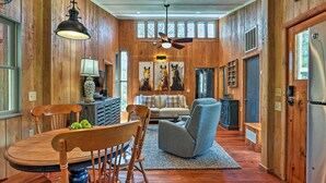 Interior em madeira com uma mesa de jantar, cadeiras, um sofá e um ventilador de teto.