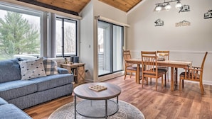 A modern living room with a wooden ceiling, a blue sofa, a dining table with chairs, and large windows. - Lincoln Escape w/ Deck: 1 Mi to Loon Mountain! (Lincoln)