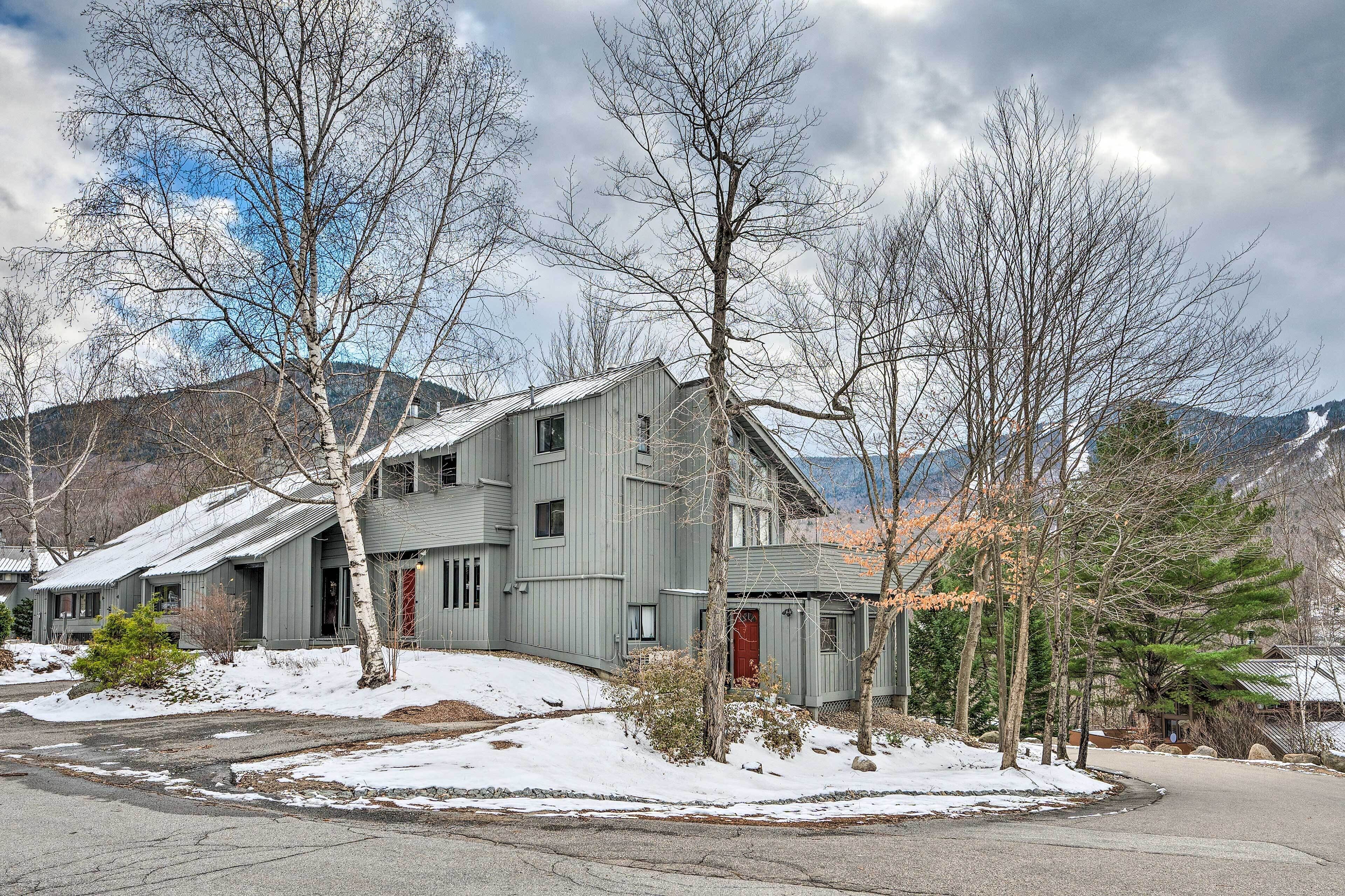 A two-story house with a sloped roof, surrounded by snow-covered ground and bare trees.