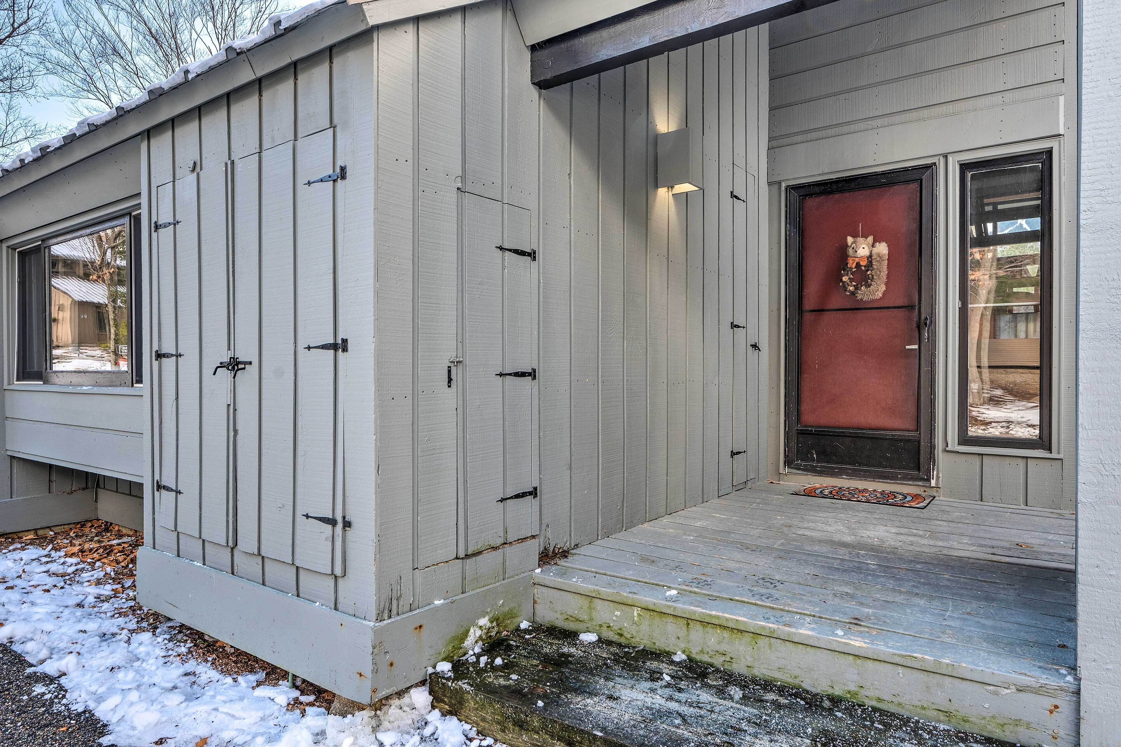Ett hus med en grå fasad, en röd dörr och en liten veranda.