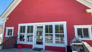 Un bâtiment rouge avec une porte et des fenêtres blanches, une terrasse en bois et un barbecue sur le côté.