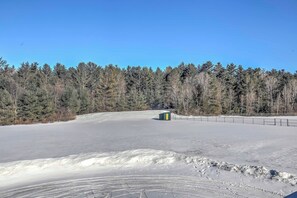 A snowy landscape with a clear sky, a fenced area, and a small structure in the distance.