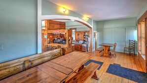 Un espace repas avec des bancs et une table en bois, une cuisine avec des meubles et des appareils électroménagers en bois, et un chambranle de porte en bois.