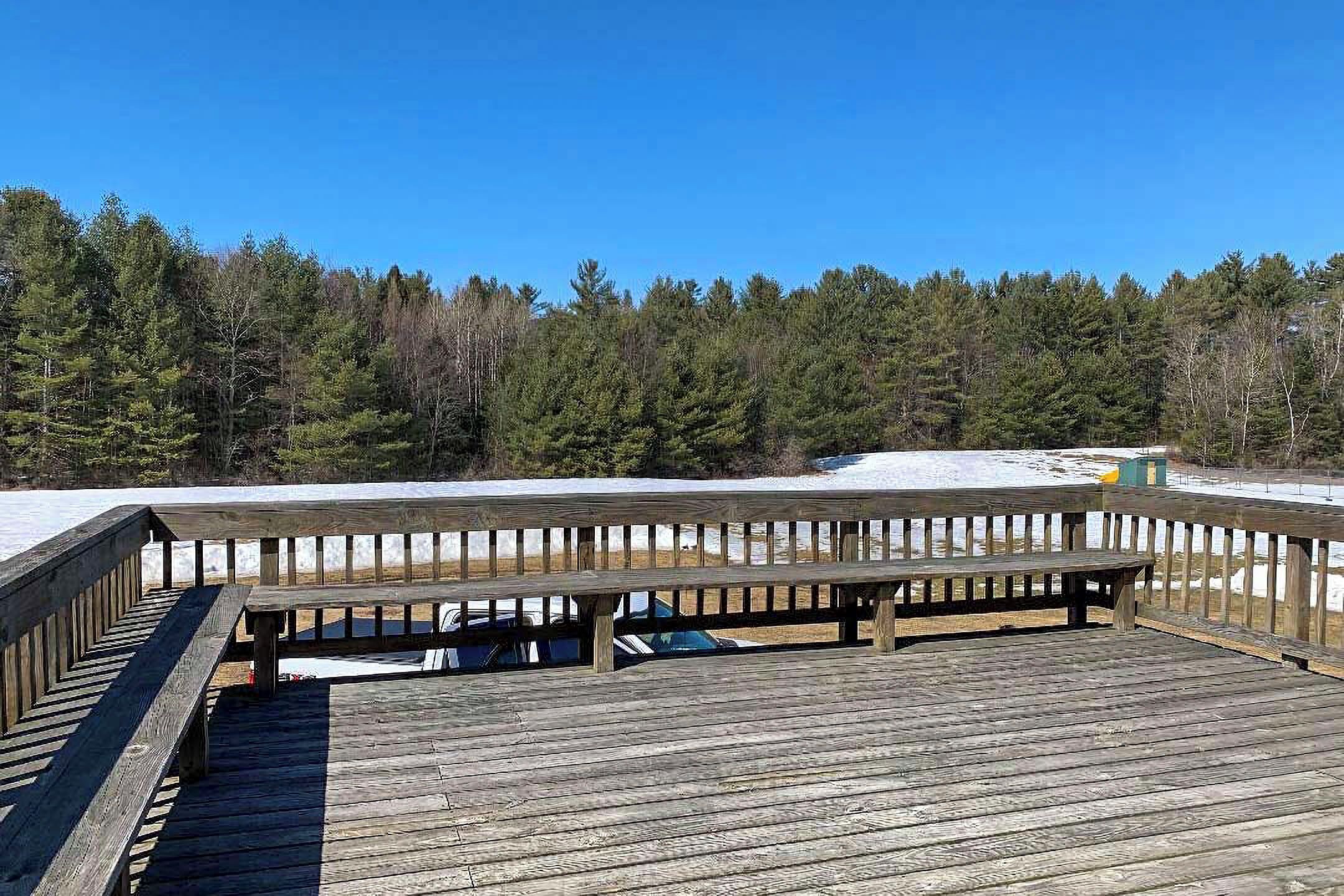 A wooden deck with benches overlooking a snowy landscape and dense forest.