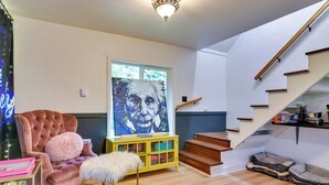 Una sala de estar con un sillón mullido, un aparador amarillo, un cuadro grande y una escalera.