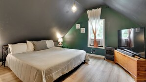 Un dormitorio con cama, mesita de noche, lámpara, televisión, calefactor y ventana con cortinas.