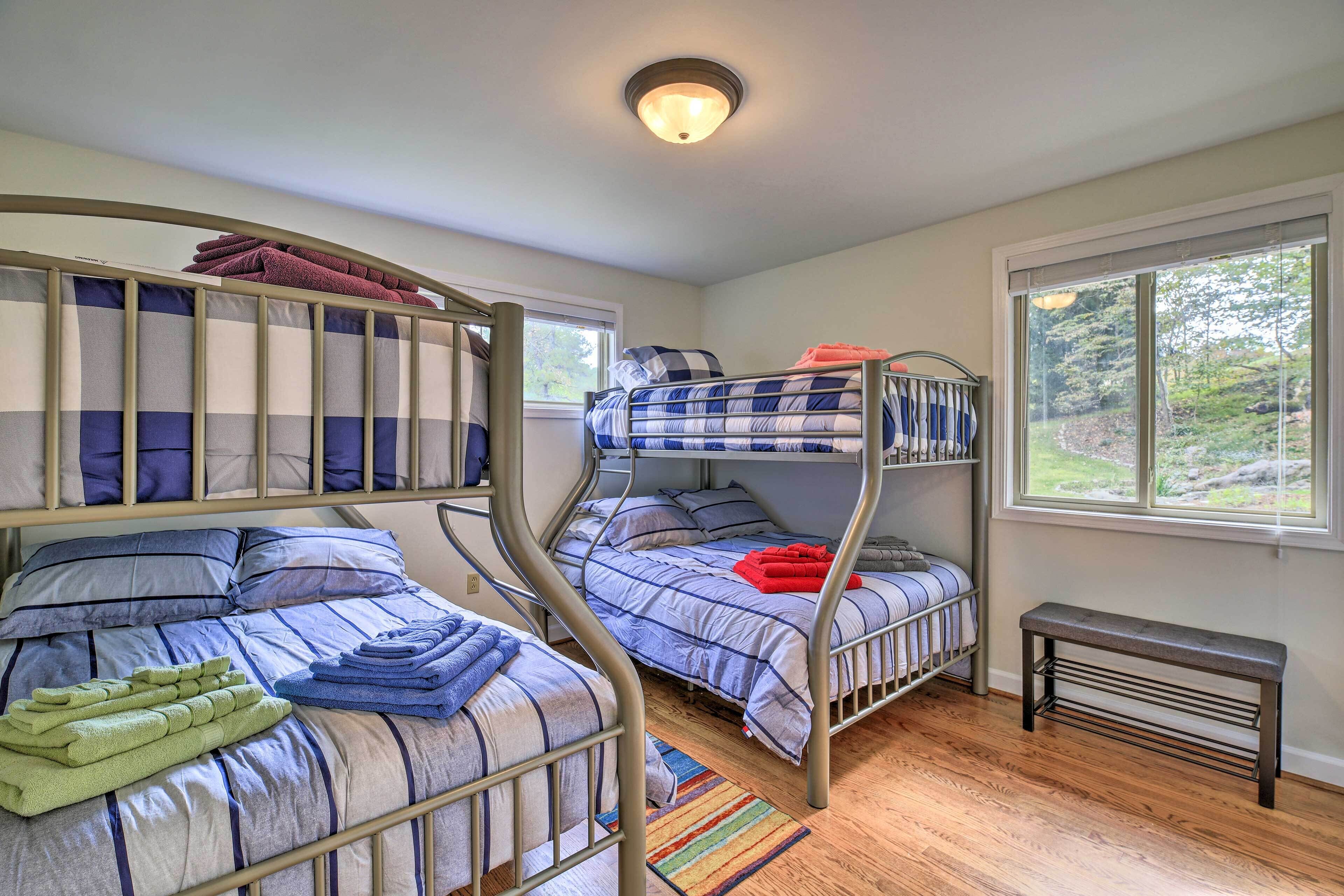 A room with bunk beds, a bench, and a window with a view of greenery.