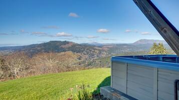 Vista desde una ventana hacia una colina cubierta de hierba y montañas al lejano.