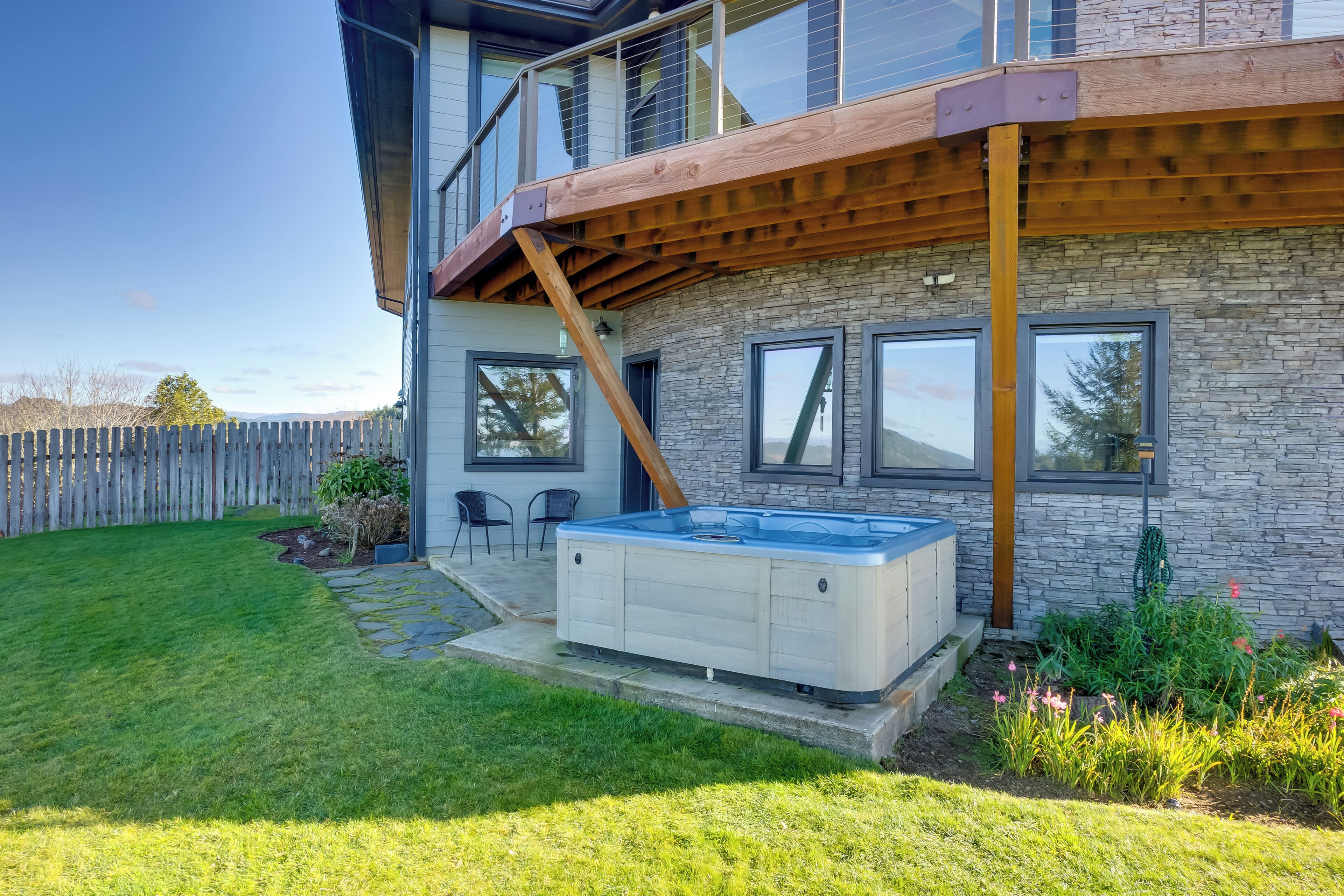 A modern house with a wooden deck, a hot tub, and a stone wall.