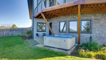 A modern house with a wooden deck, a hot tub, and a stone wall.