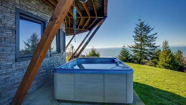 A hot tub outside a stone building with a wooden roof and a view of the ocean. - Stunning 360 Ocean Views, Near Redwoods NP! (Smith River)