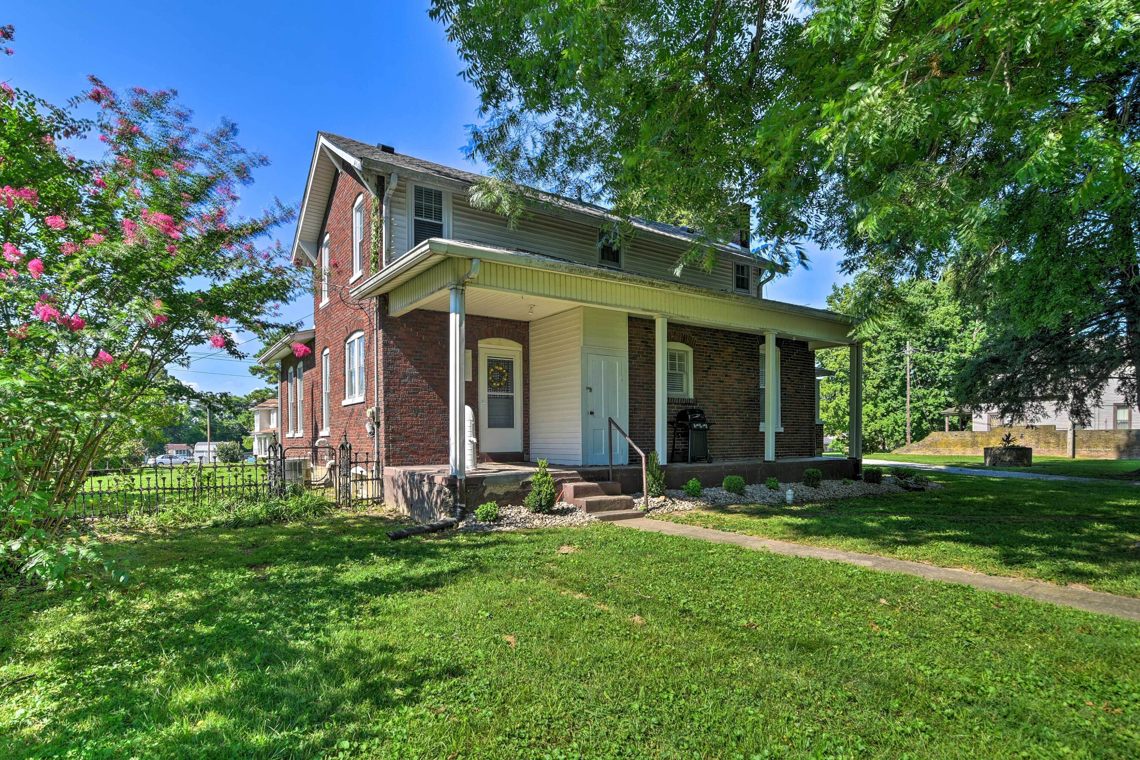 A two-story brick house with a front porch, a small front yard, and a tree with pink flowers.