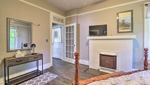 A bedroom with a wooden bed, a fireplace, a TV, and a console table with a mirror and lamp. - Glasgow Home w/ Porch: Close to Lake & Caves! (Glasgow)