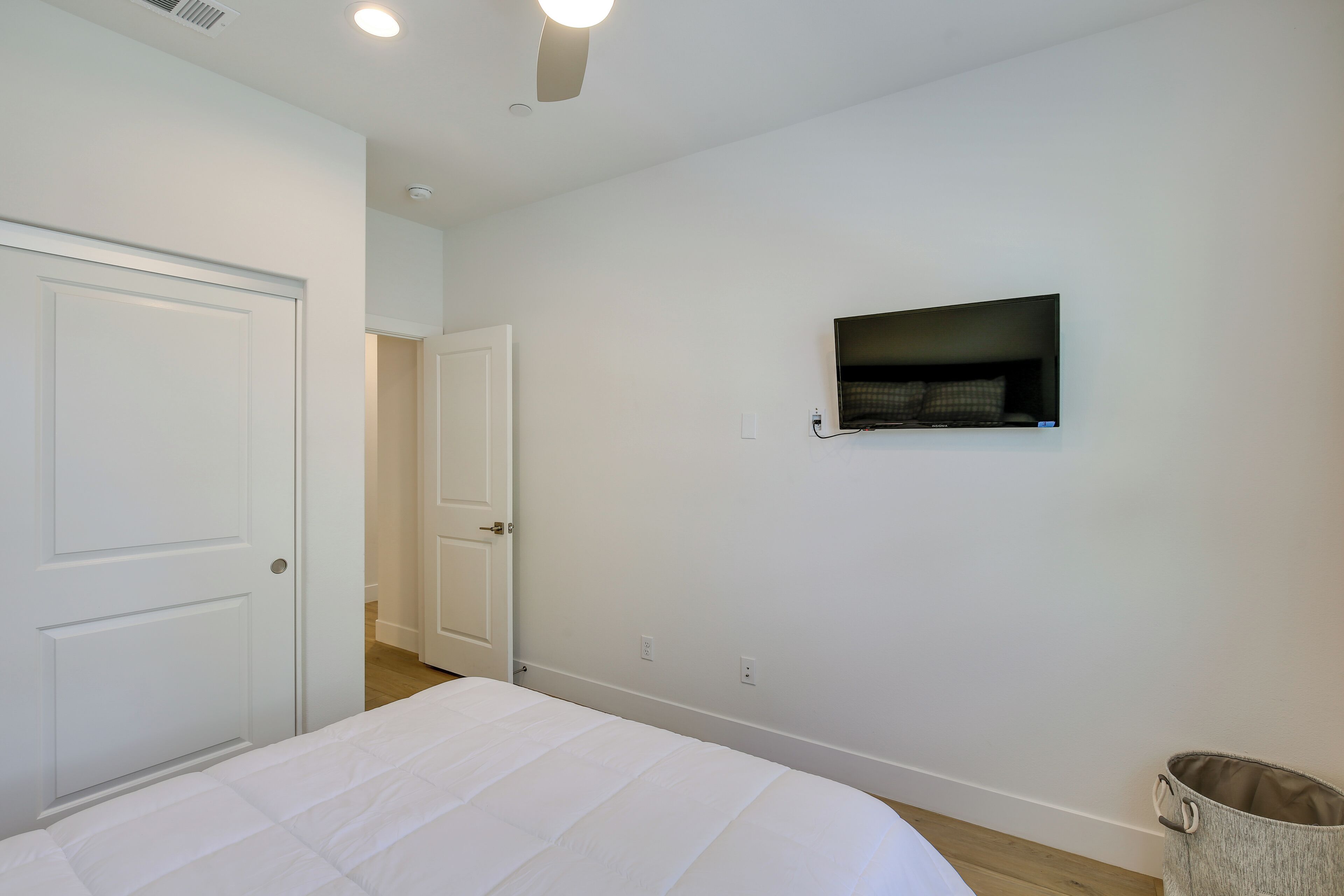 A bedroom with a bed, a television mounted on the wall, and a door leading to another room.