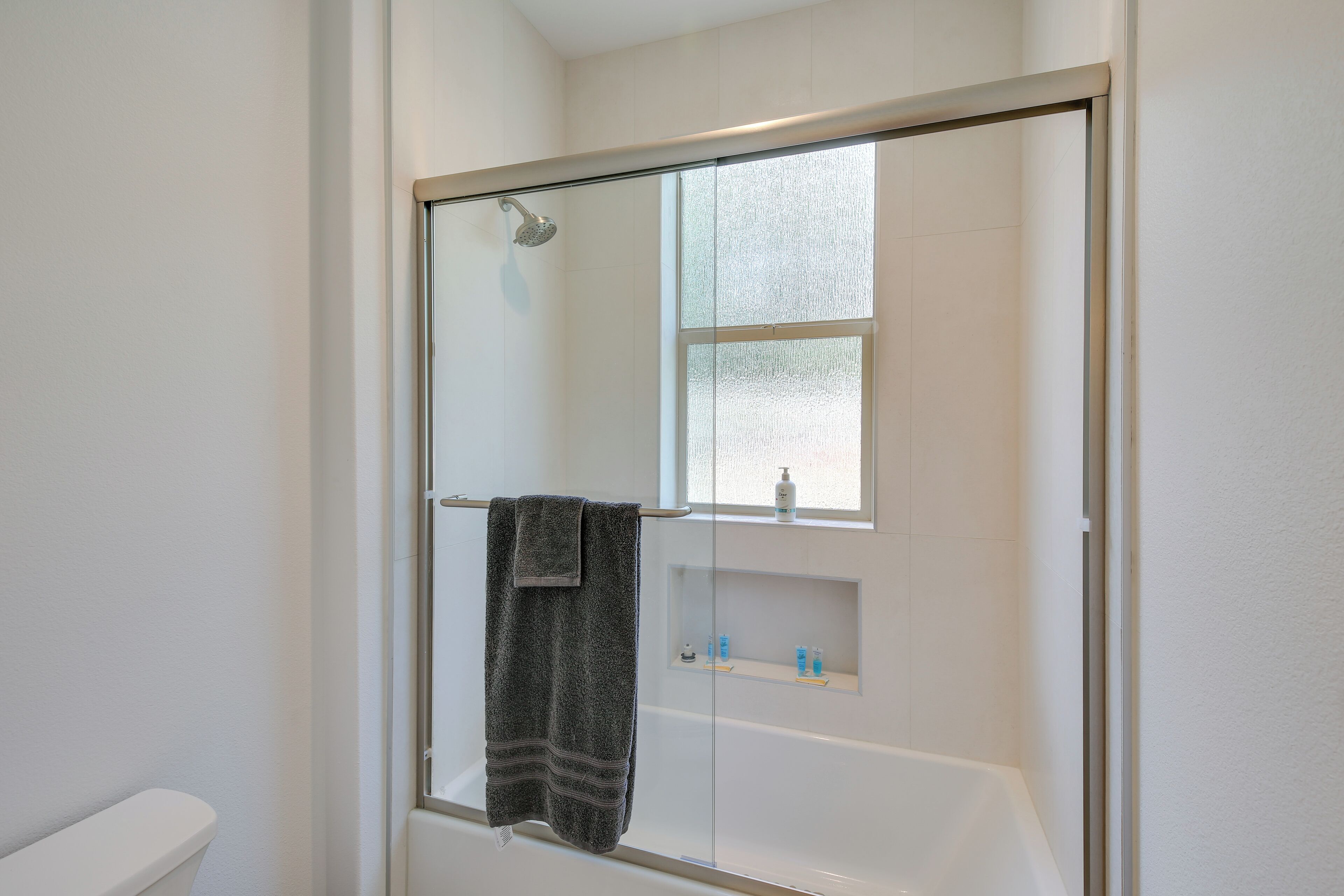 A bathroom with a glass-enclosed shower, a white bathtub, and a window above the sink.